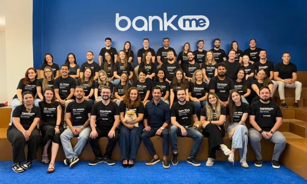 Equipe da Bankme reunida no escritório para foto oficial em frente à logo da empresa.