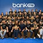 Equipe da Bankme reunida no escritório para foto oficial em frente à logo da empresa.